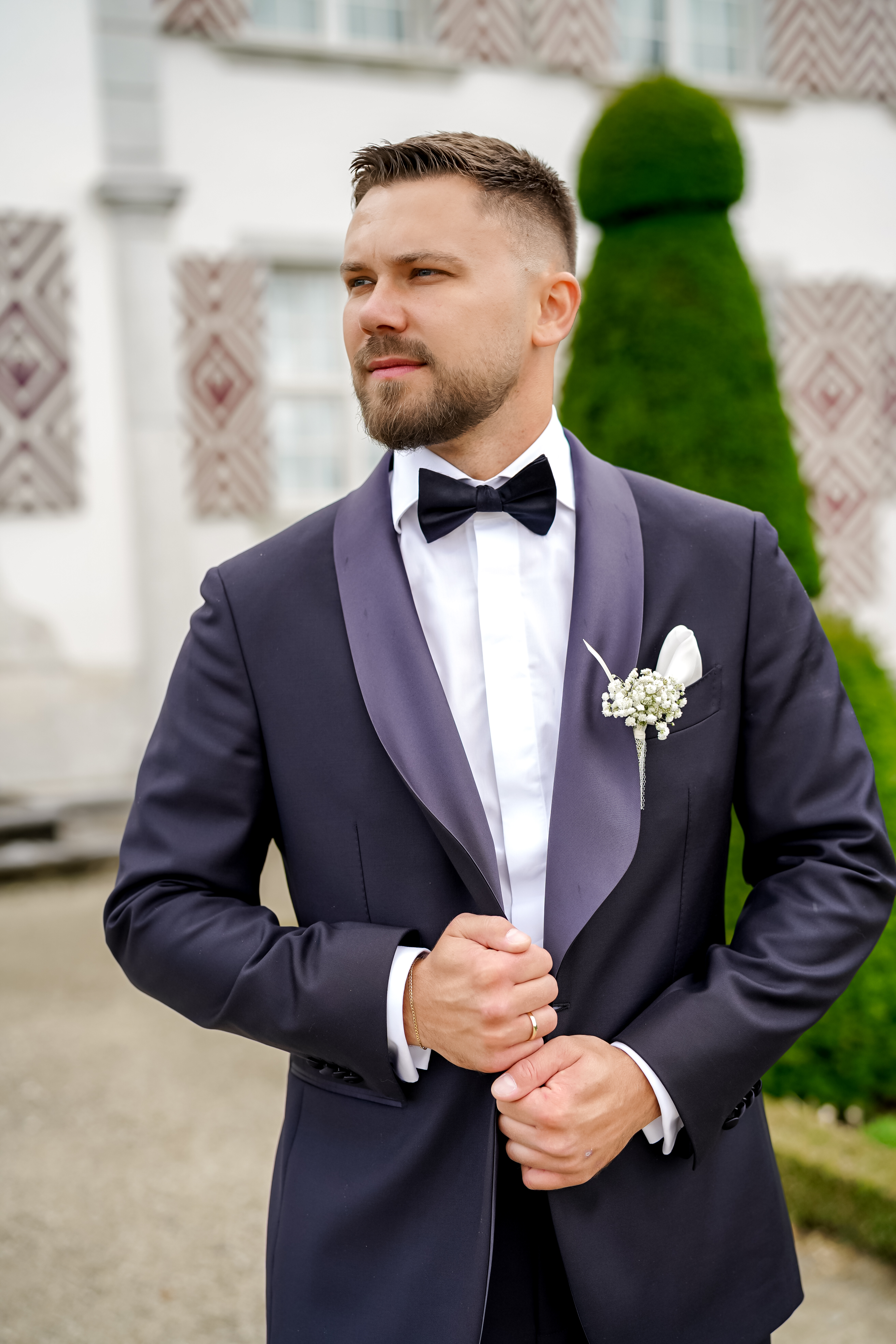 Portret i një burri me smoking të errët, këmishë të bardhë dhe papion, duke pozuar jashtë.